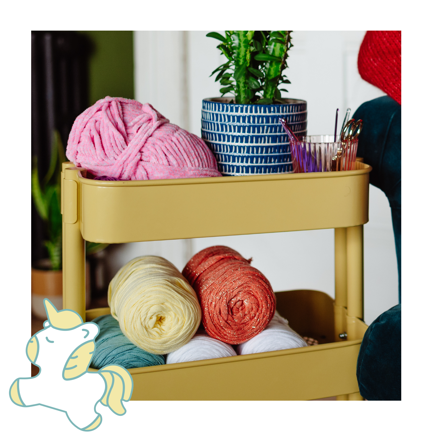 Yellow cart with colorful yarn and a plant on a white background